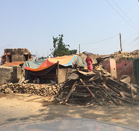 A village woman stands on the pile of rubble of what was once her home